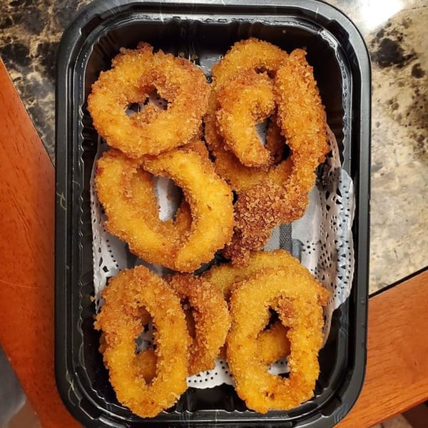 Golden-brown fried calamari rings, served in a black takeout container with a white doily liner.