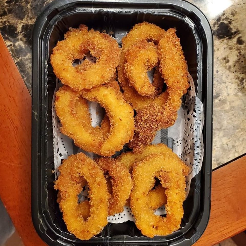 Golden-brown fried calamari rings, served in a black takeout container with a white doily liner.